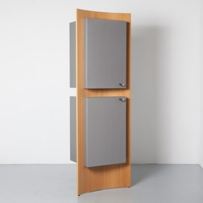 Postmodern vertical cabinet two cubes pushed through a curved panel oak wood veneer space-grey pearlescent silver finish one mirror upper other mini-fridge bar lower cupboard closet storage 1990s nineties shelf shelves door